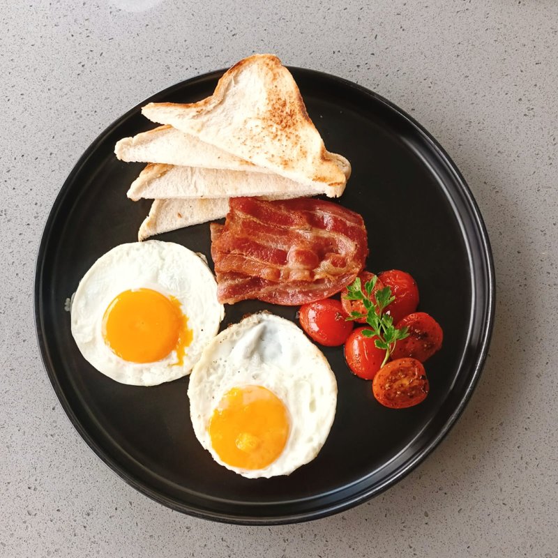Breakfast with eggs, bacon, tomatoes and toast on a black plate