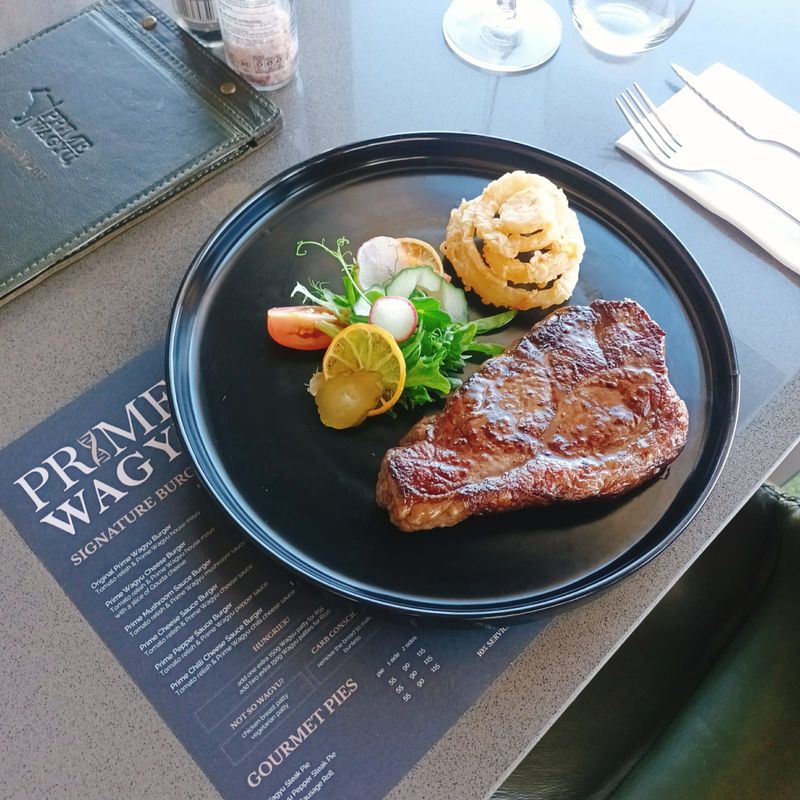 A grilled steak served with onion rings and salad on a black plate