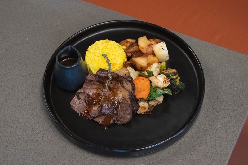 A plated roast with potatoes, vegetables, rice and a small jug of gravy